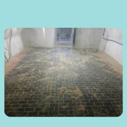 Jan Chmielarz - Układanie cegieł na podłodze w trakcie prac remontowych, widoczne resztki zaprawy i pył.