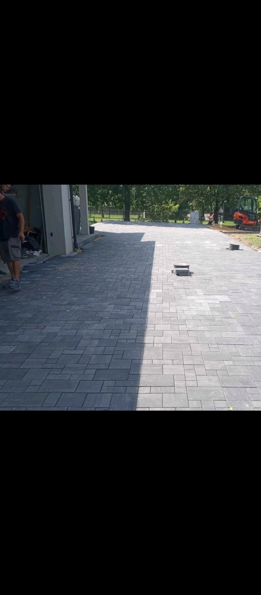 Ułożona szara kostka brukowa na podjeździe, z widocznym mini-koparką w tle i fragmentem budynku w trakcie prac wykończeniowych.