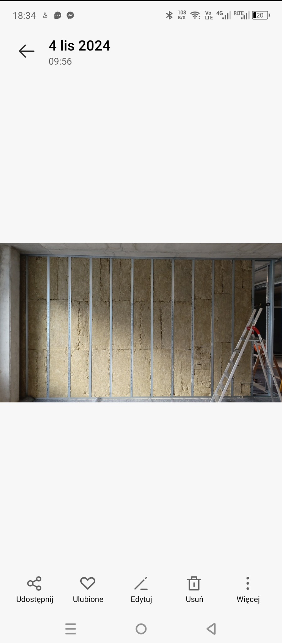 Ściana z metalowym stelażem wypełnionym wełną mineralną, widoczna drabina oparta o ścianę, etap prac wykończeniowych.