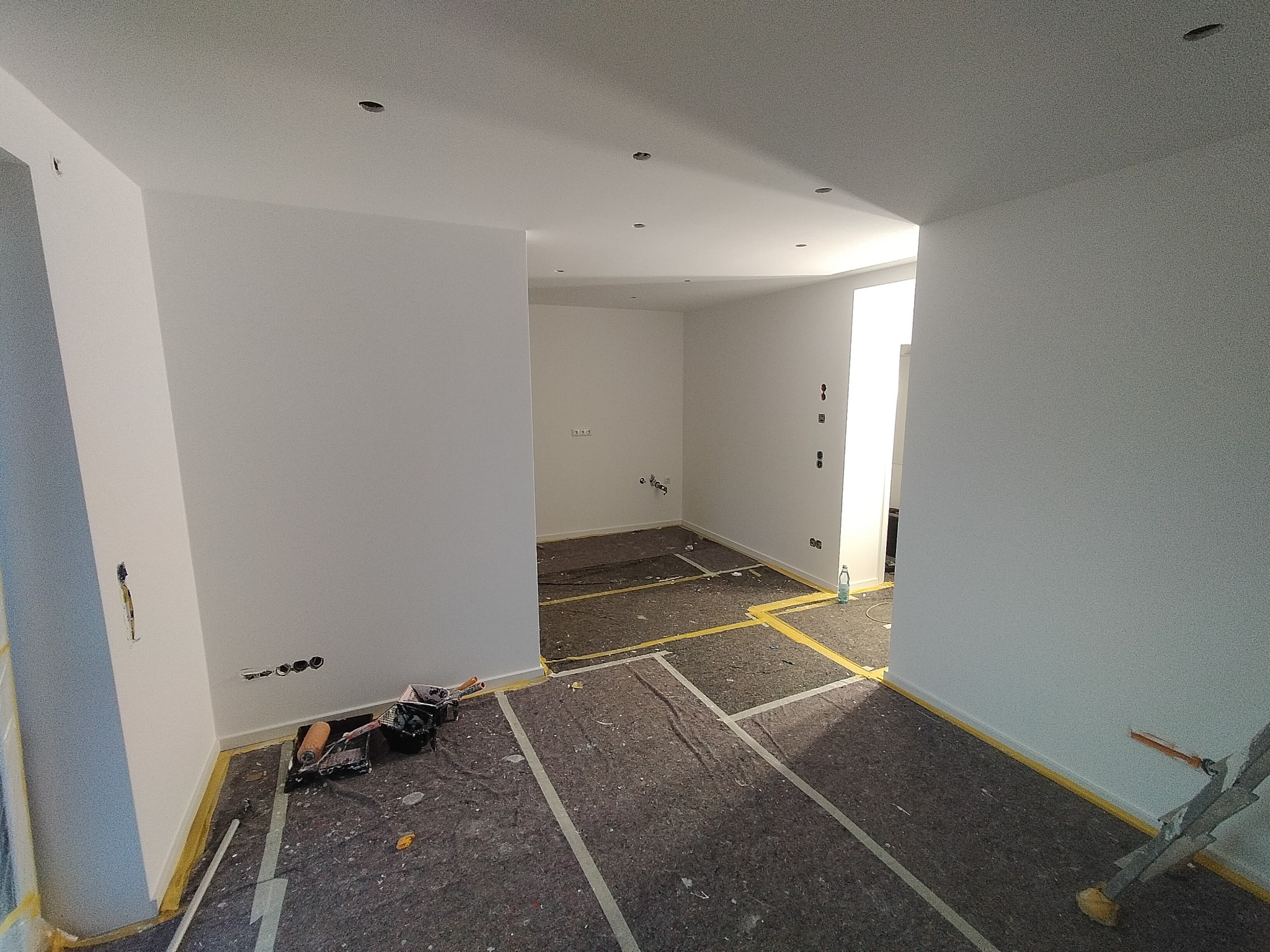 Wnętrze po malowaniu na biało, zabezpieczona podłoga, widoczne narzędzia malarskie i drabina.