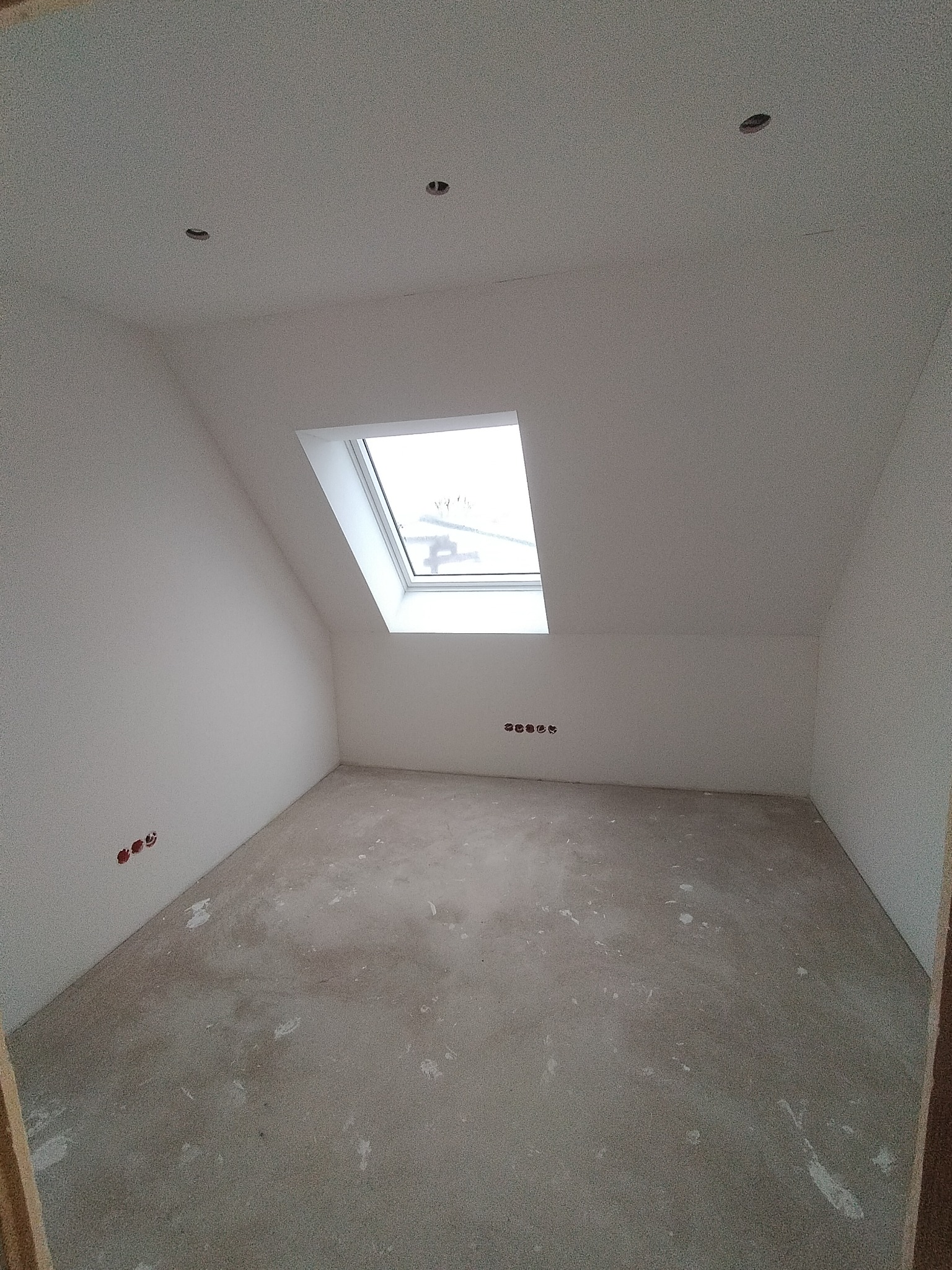 Poddasze w stanie deweloperskim z oknem dachowym, widoczne ślady po gładzi na ścianach i wylewce podłogowej, przygotowane do dalszych prac wykończeniowych.