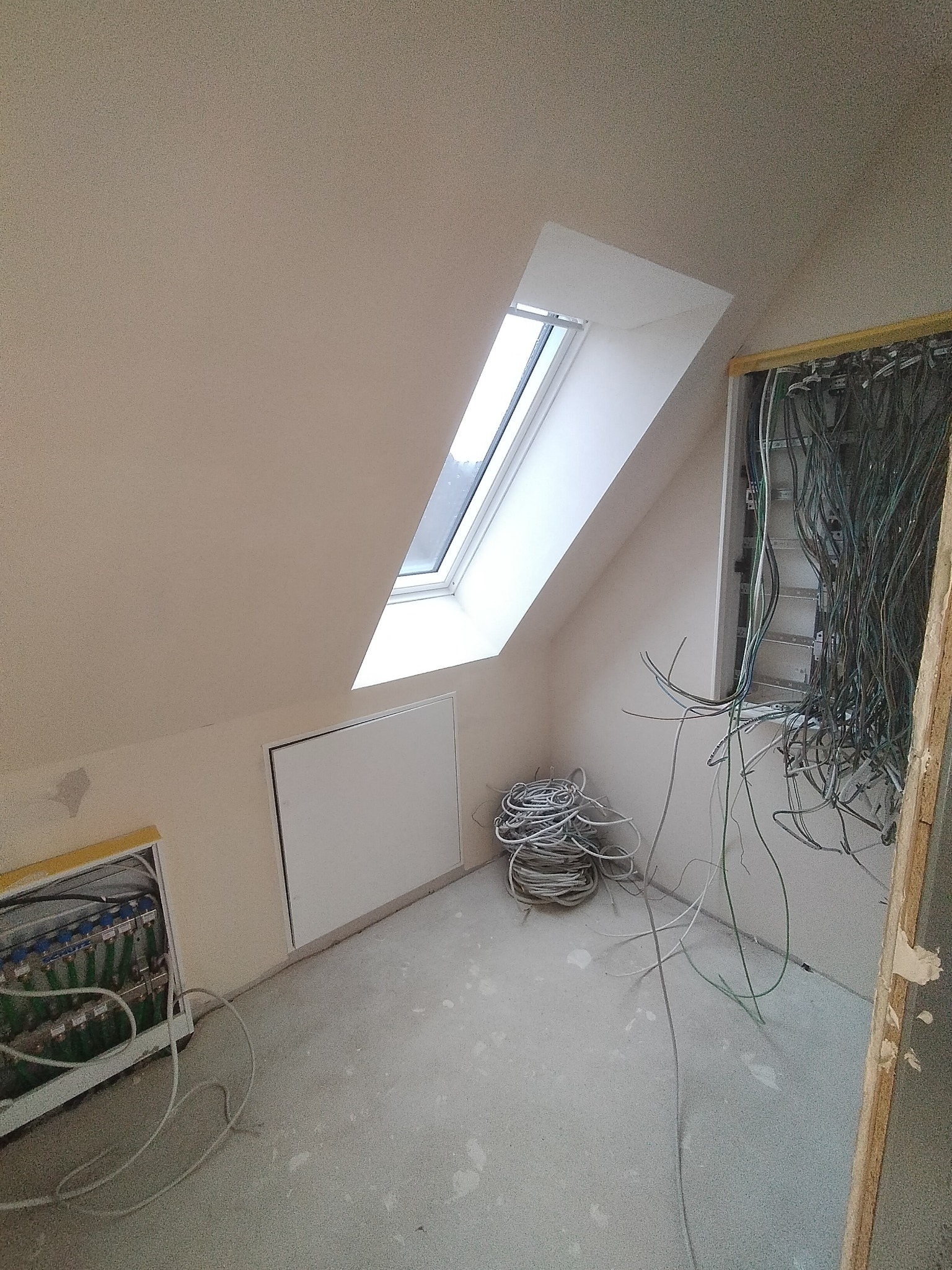 Poddasze w Kętrzynie w trakcie prac wykończeniowych: widoczne okno dachowe, niezabudowana skrzynka elektryczna z licznymi przewodami oraz przygotowane kable zwinięte w kłębek na podłodze.