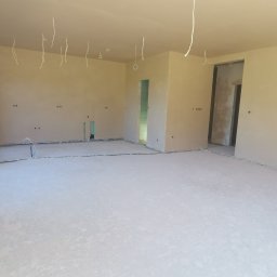 ART-INVEST Damian Solarski - Surowe wnętrze w trakcie wykańczania: ściany po nałożeniu tynku, widoczne kable elektryczne wystające ze ścian i sufitu, przygotowana podłoga, brak wykończenia w otworach drzwiowych.