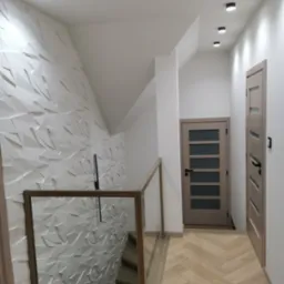 Nowoczesne wnętrze z trójwymiarową białą ścianą, drewnianą balustradą schodów ze szkłem, parkietem w jodełkę i dwiema beżowymi parami drzwi.