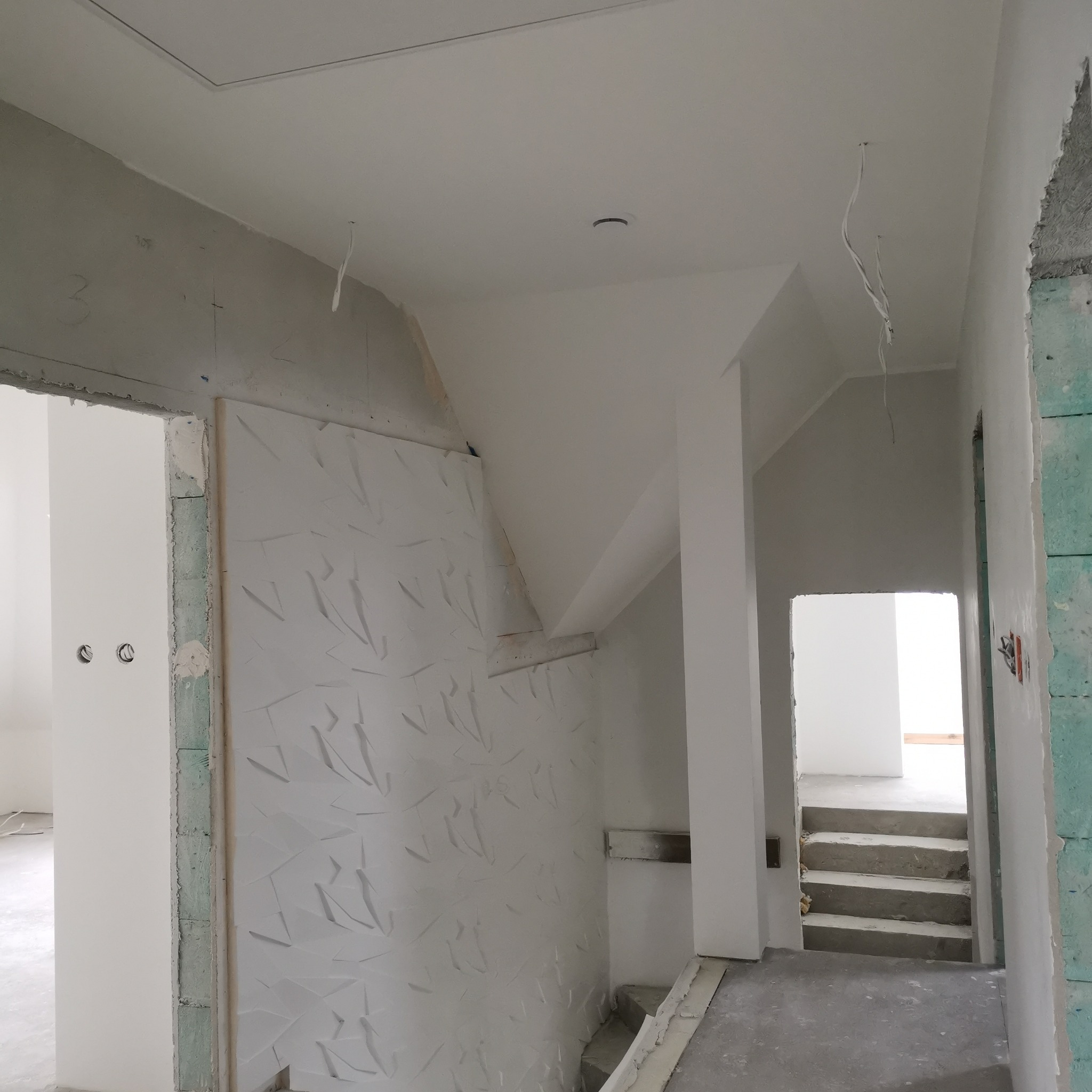 Nowoczesne wykończenie wnętrza: białe ściany z dekoracyjną fakturą, surowy beton na podłodze i schodach, widoczne kable elektryczne, sufit z otworem inspekcyjnym.