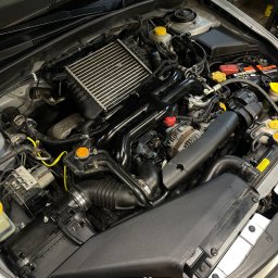 B44 Serwis - Widok z góry na otwartą maskę srebrnego samochodu z widocznym silnikiem, akumulatorem i innymi komponentami, z żółtymi akcentami na korkach i przewodach.