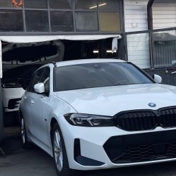 B44 Serwis - Białe BMW serii 3 stoi przed warsztatem z otwartą maską innego białego SUV-a w tle, widoczne logo BMW na masce.