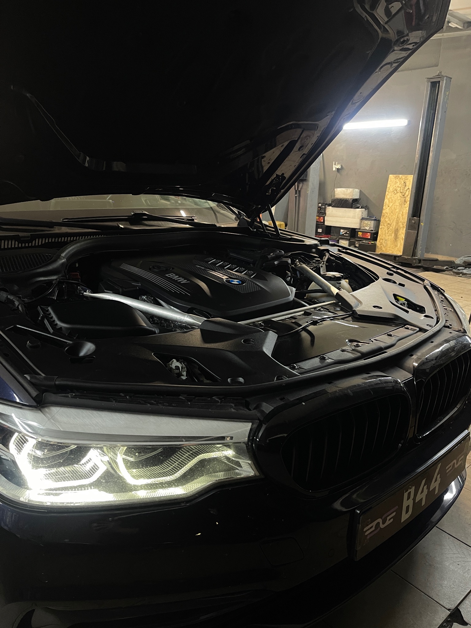 Czarny samochód BMW z otwartą maską w warsztacie, widoczny silnik i reflektory, tablica rejestracyjna B44