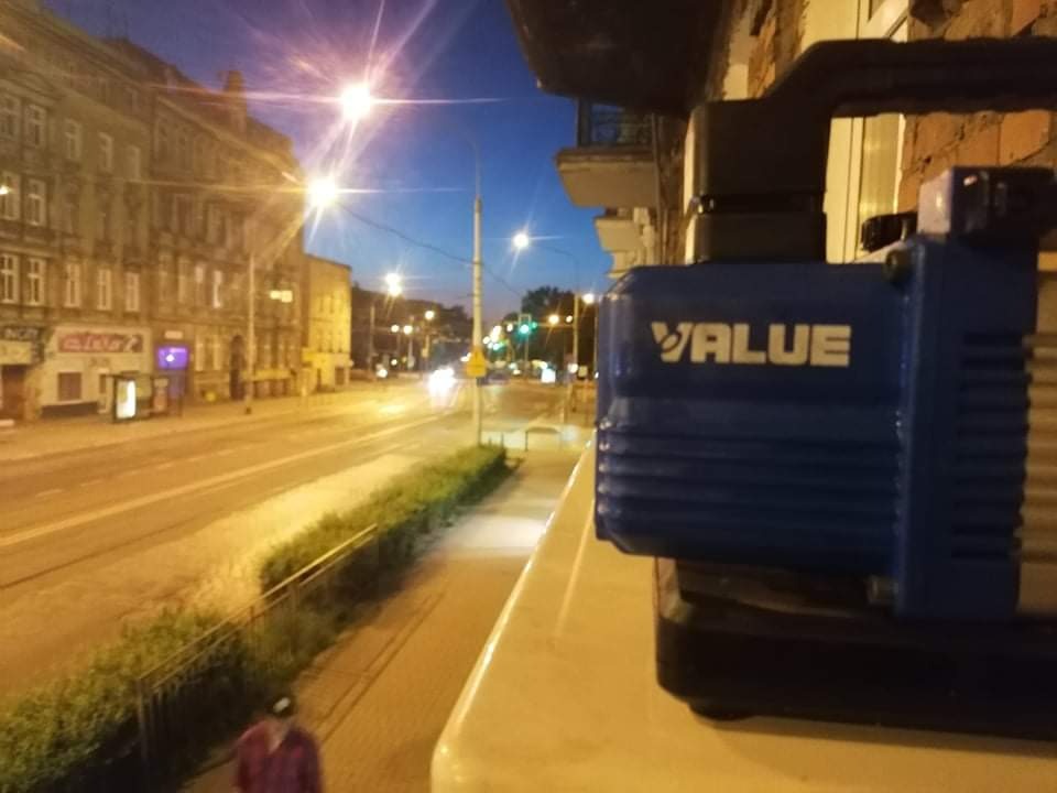 Niebieska pompa próżniowa marki VALUE na balkonie z widokiem na nocną ulicę miasta, z budynkami w stylu kamienic i oświetleniem ulicznym.