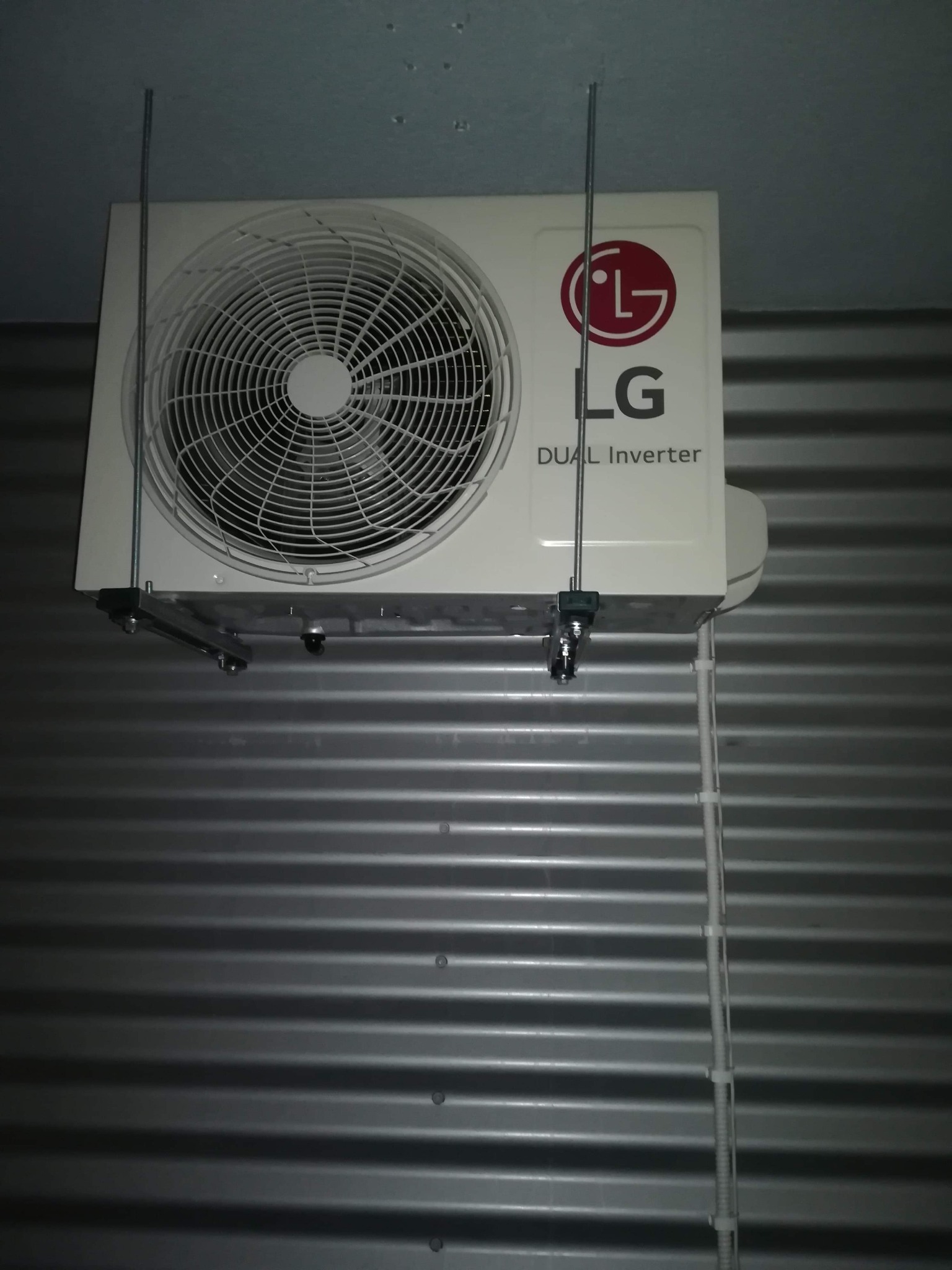 Zewnętrzna jednostka klimatyzacji LG Dual Inverter zamontowana na szarej, falistej ścianie we Wrocławiu, widoczne metalowe wsporniki i przewody.