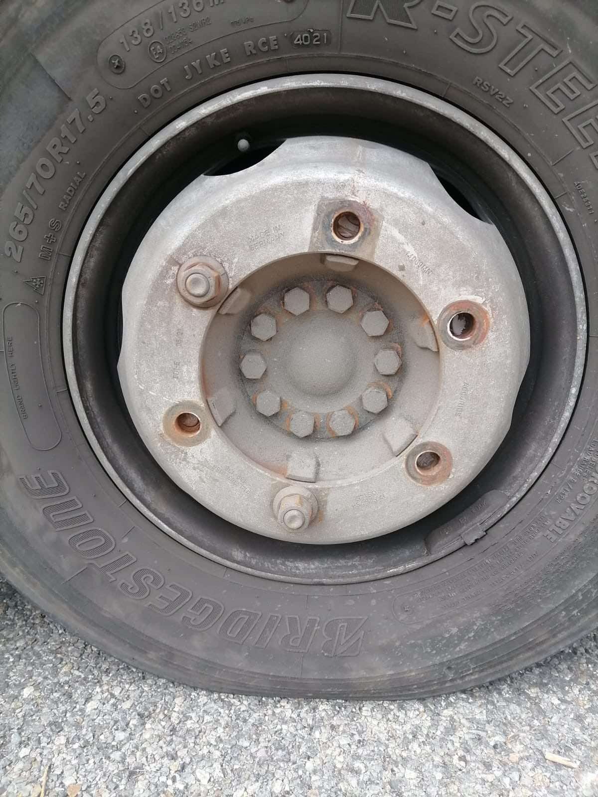 Ciężarowe koło Bridgestone 265/70R17.5 z szarą felgą i wystającymi śrubami, widoczne oznaczenia na oponie i ślady użytkowania.