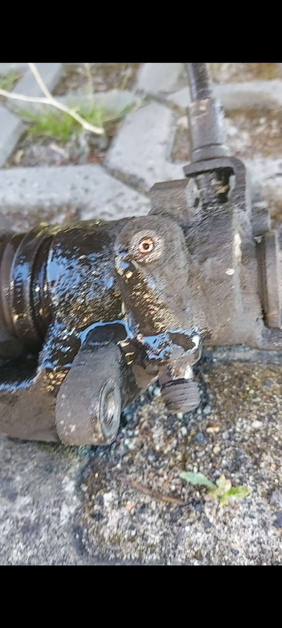 Brudny, zużyty element zawieszenia samochodowego, prawdopodobnie po demontażu, leżący na betonowej powierzchni.