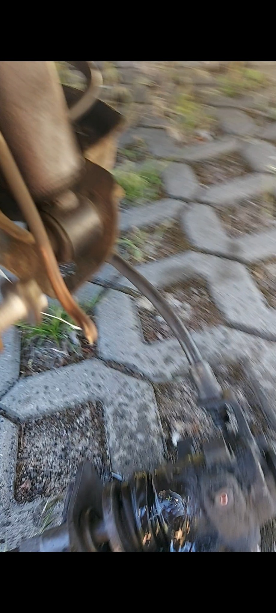 Nisko kątowe ujęcie podwozia pojazdu z widocznymi elementami zawieszenia na tle betonowej kostki brukowej i trawy.