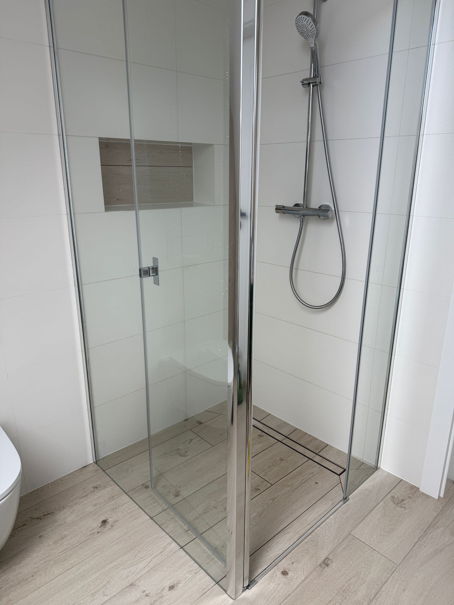 Nowoczesna kabina prysznicowa z chromowanymi profilami i deszczownicą, w tle białe płytki i drewnopodobna wnęka, Kobierzyce.