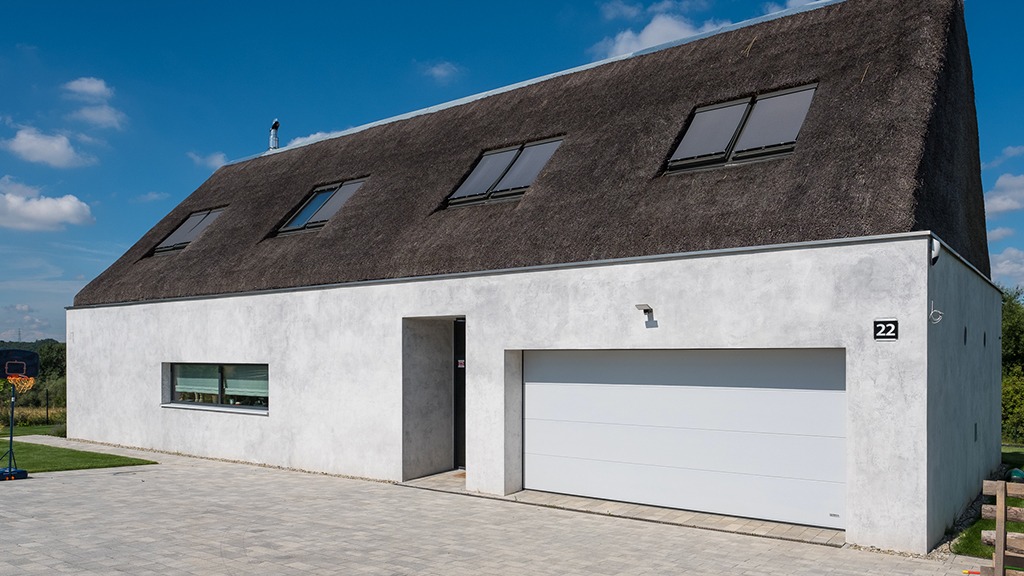 Nowoczesny dom z białym tynkiem, strzechą na dachu, oknami dachowymi z roletami i białą bramą garażową segmentową, numer posesji 22.