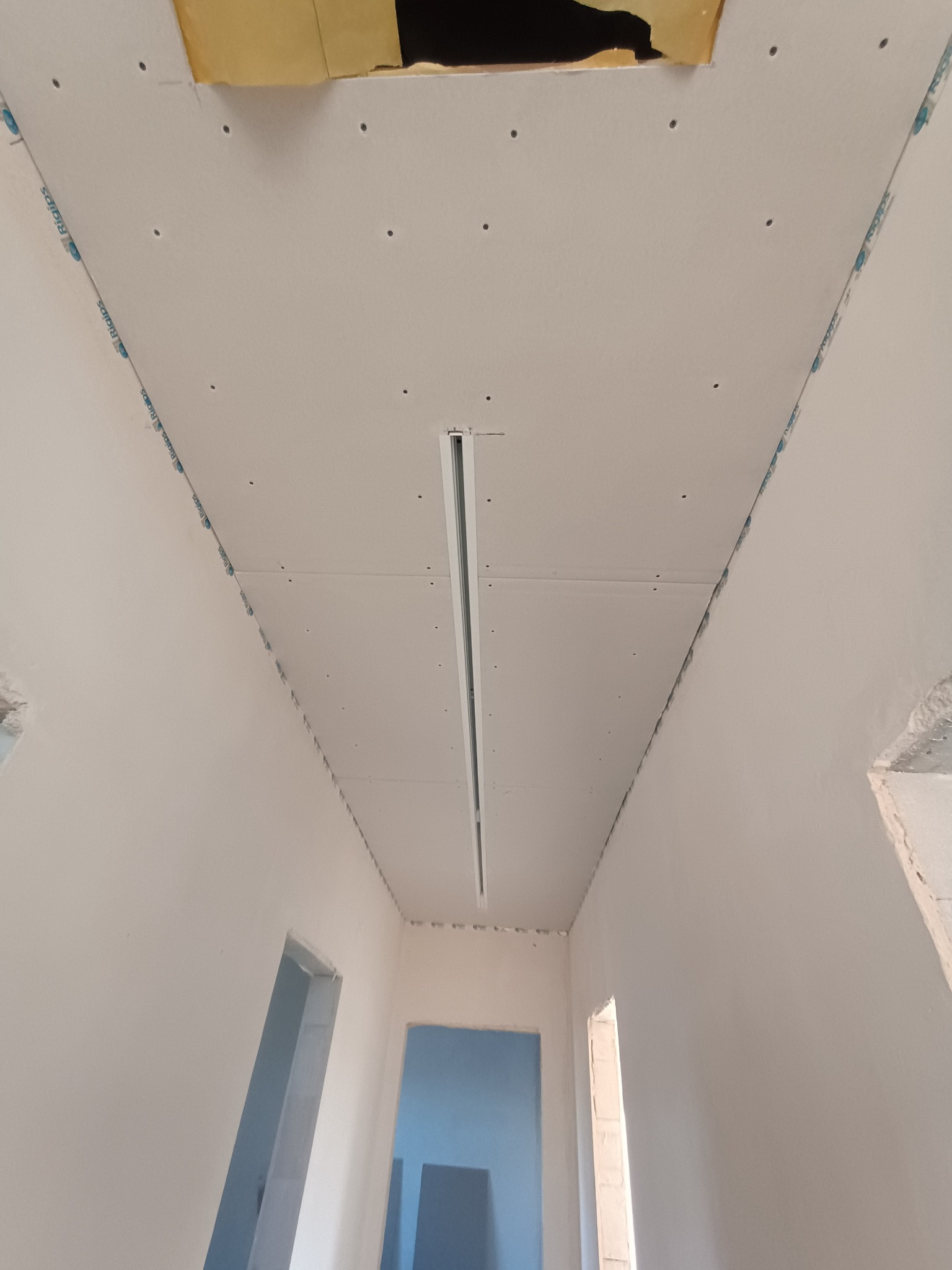 Sufit podwieszany z płyt gipsowo-kartonowych w trakcie montażu, widoczne profile i otwory na oświetlenie. Ujęcie z dołu, surowe ściany w tle.