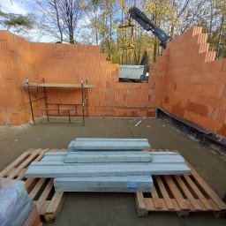 BMV MS - Wznoszenie ścian z pustaków ceramicznych w Bielsko-Białej, widoczny dźwig dostarczający materiał, paleta z prefabrykatami betonowymi na pierwszym planie.