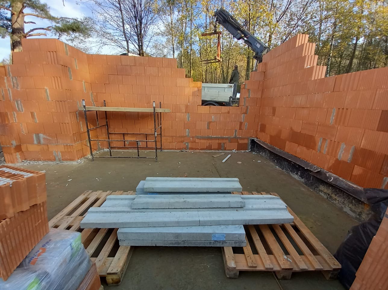 Wznoszenie ścian z pustaków ceramicznych w Bielsko-Białej, widoczny dźwig dostarczający materiał, paleta z prefabrykatami betonowymi na pierwszym planie.