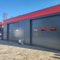 EIFAM Mateusz Nowacki - Dwie szare bramy segmentowe z czerwonymi nadprożami, widoczne okienka w bramach, na pierwszym planie kostka brukowa, obok bramy leżą narzędzia ogrodnicze.