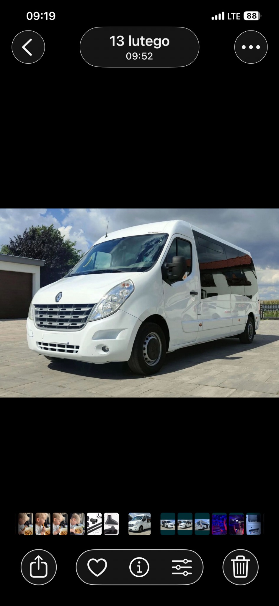 Biały bus Renault Master z przyciemnianymi szybami, zaparkowany na betonowym placu w słoneczny dzień. Widok z boku, zarys budynku w tle.