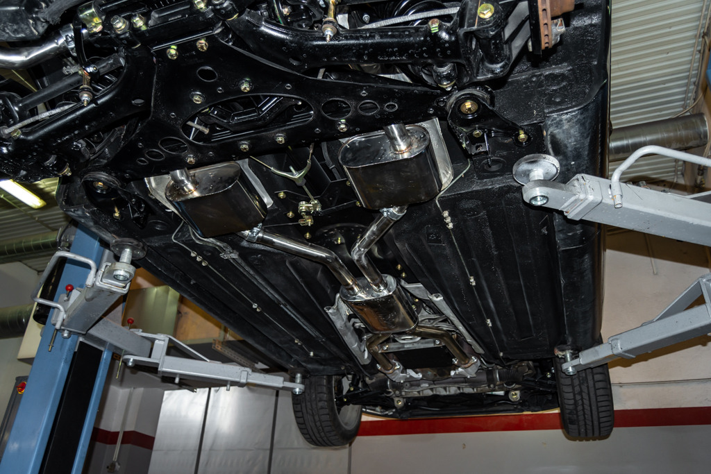 Podwozie samochodu na podnośniku, widoczne nowe, błyszczące elementy układu wydechowego oraz elementy zawieszenia pomalowane na czarno.