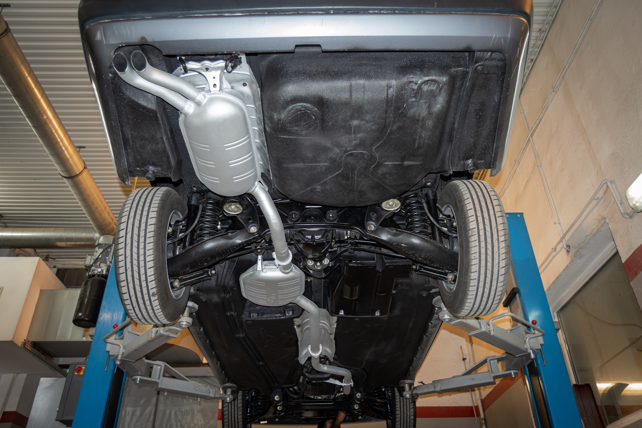 Podwozie samochodu po zabezpieczeniu antykorozyjnym, widoczne nowe elementy układu wydechowego, auto na podnośniku warsztatowym.