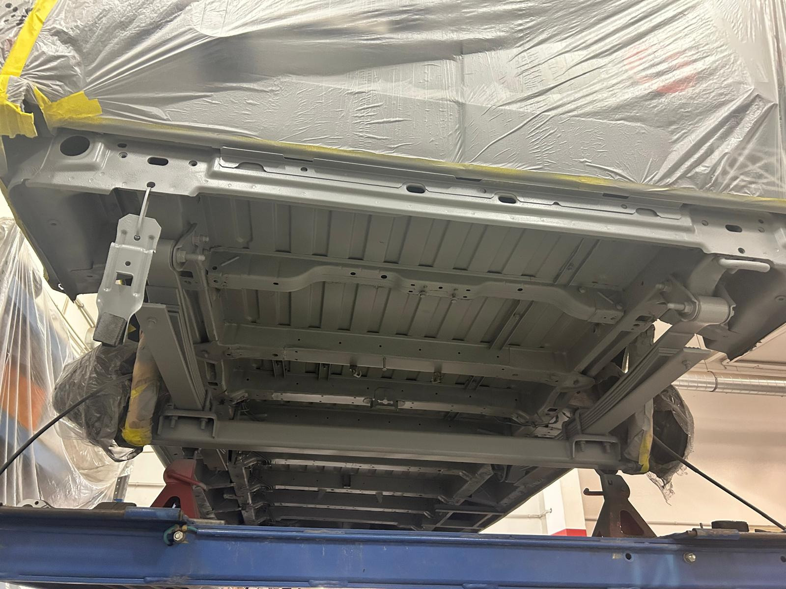 Podwozie samochodu na podnośniku, po piaskowaniu i zabezpieczeniu antykorozyjnym, częściowo zamaskowane folią i taśmą malarską, gotowe do lakierowania.