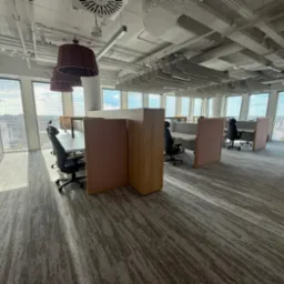 Nowoczesne biuro z widocznymi instalacjami pod sufitem, oświetleniem i stanowiskami pracy. Widok z perspektywy podłogi, ukazujący estetykę i funkcjonalność przestrzeni.