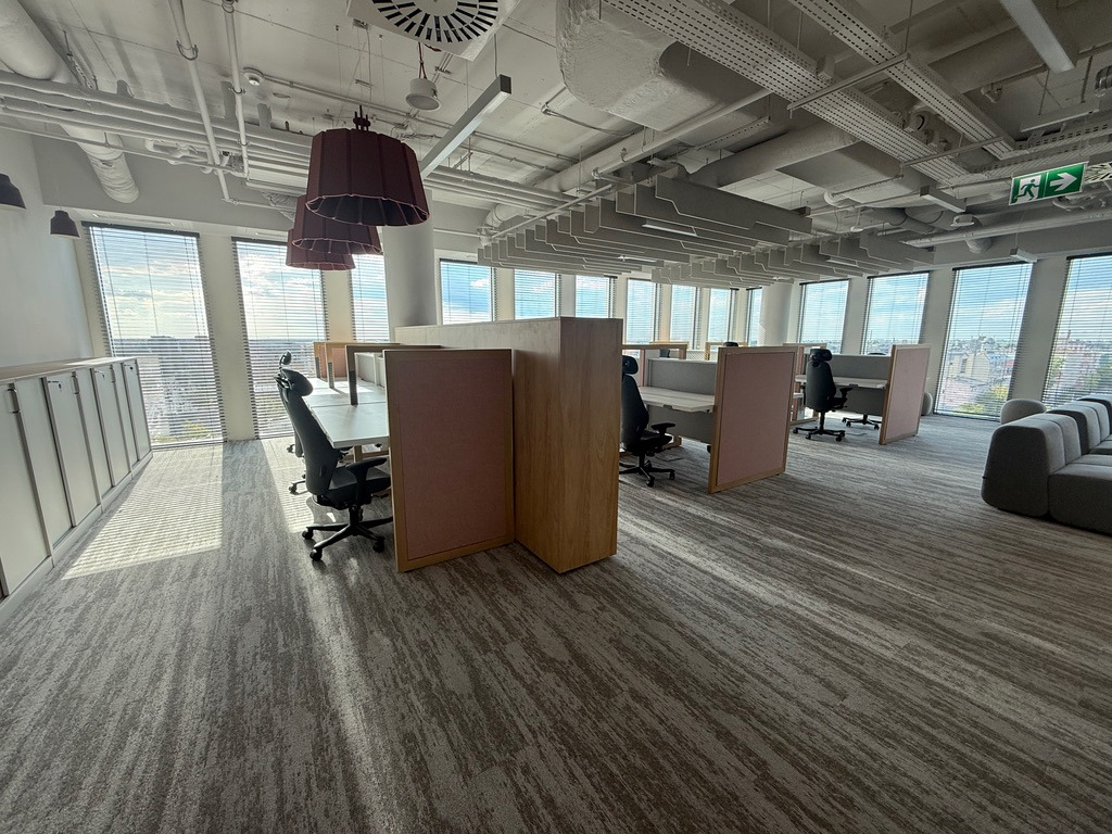 Nowoczesne biuro z widocznymi instalacjami pod sufitem, oświetleniem i stanowiskami pracy. Widok z perspektywy podłogi, ukazujący estetykę i funkcjonalność przestrzeni.