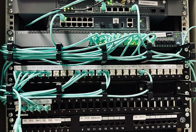 Serwerownia z panelami krosowniczymi, switchami Juniper i okablowaniem kategorii 6 w kolorze turkusowym, uporządkowanym za pomocą opasek. Widok z bliska.