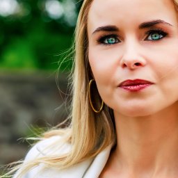 MAR-MAL Mariusz Piórkowski - Portret kobiety o blond włosach i intensywnym makijażu oczu, z zielonym tłem w tle. Widoczne złote kolczyki koła i biała marynarka.