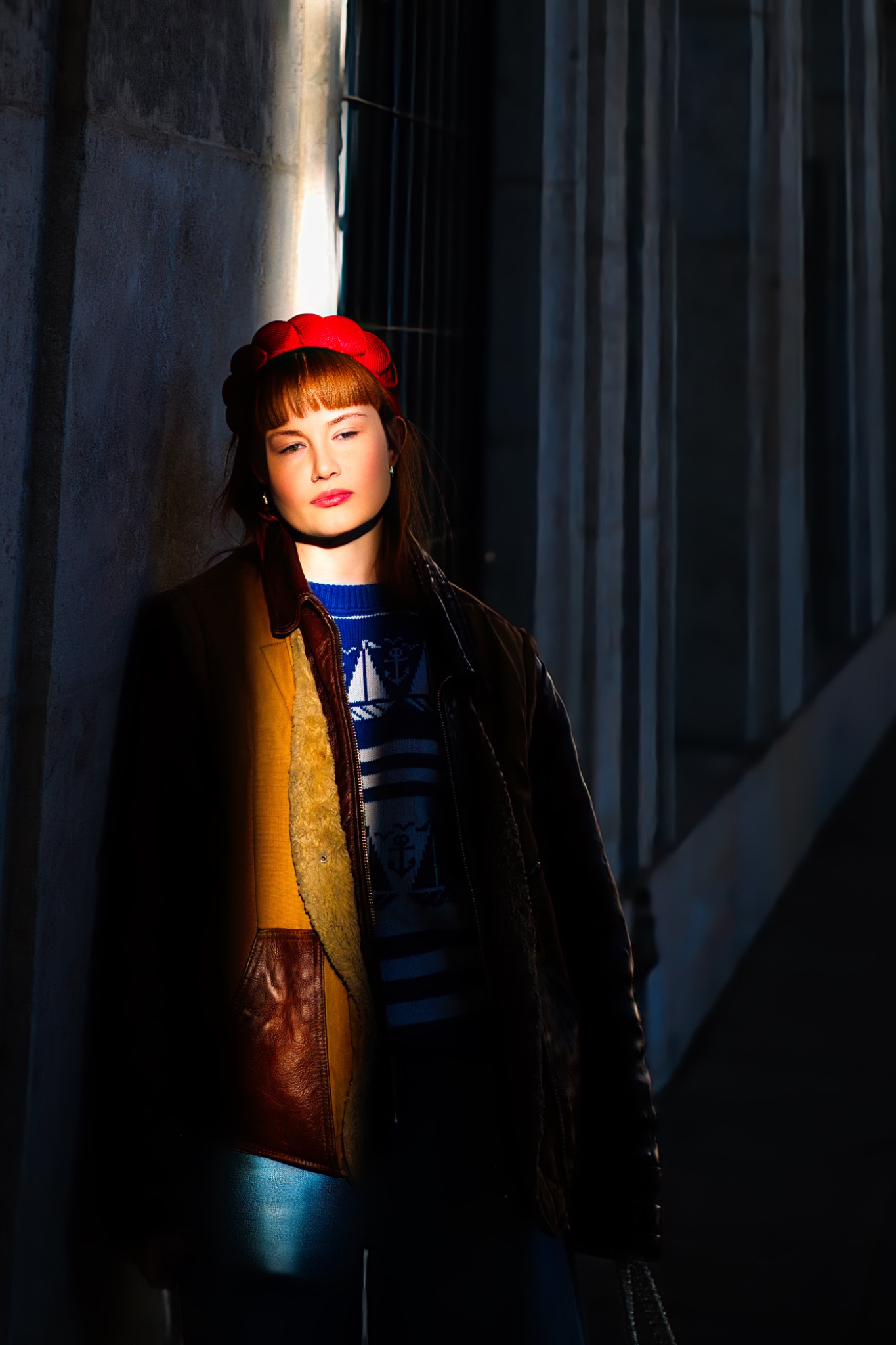 Portret kobiety w czerwonym berecie, oświetlonej mocnym światłem na tle betonowej ściany i metalowej konstrukcji, w stylistyce sesji kobiecej.