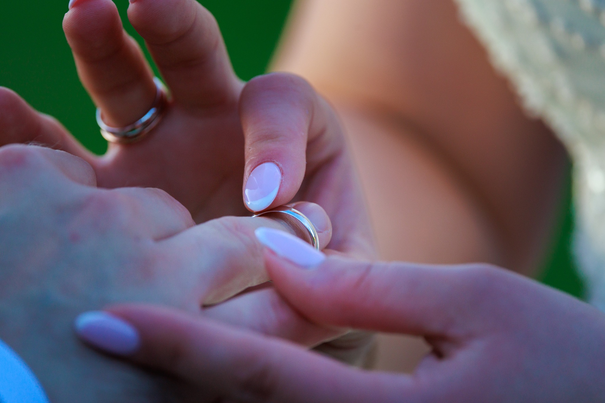 Dłonie pary młodej podczas ceremonii ślubnej, zbliżenie na zakładanie obrączki, delikatny manicure panny młodej, zielone tło.