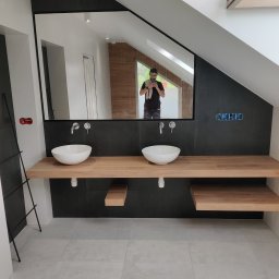 REMONT Z PASJĄ SZYMON KRZUS - Nowoczesna łazienka na poddaszu z czarnymi płytkami, drewnianym blatem pod umywalki i dużym lustrem, w którym odbija się osoba robiąca zdjęcie telefonem.