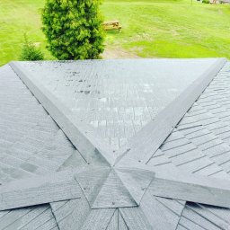 REMONT Z PASJĄ SZYMON KRZUS - Widok z góry na szary dach altany pokryty kroplami deszczu, z zielonym trawnikiem i drzewami w tle.