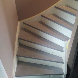 REMONT Z PASJĄ SZYMON KRZUS - Drewniane schody wewnętrzne po malowaniu, z szarymi stopniami i białymi podstopnicami, widoczne ślady świeżej farby i taśma malarska zabezpieczająca.