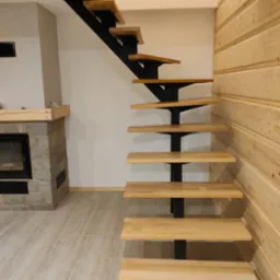 Nowoczesne, drewniane schody jednobiegowe z czarną, metalową konstrukcją, umieszczone w pomieszczeniu z drewnianą boazerią i kamiennym kominkiem.