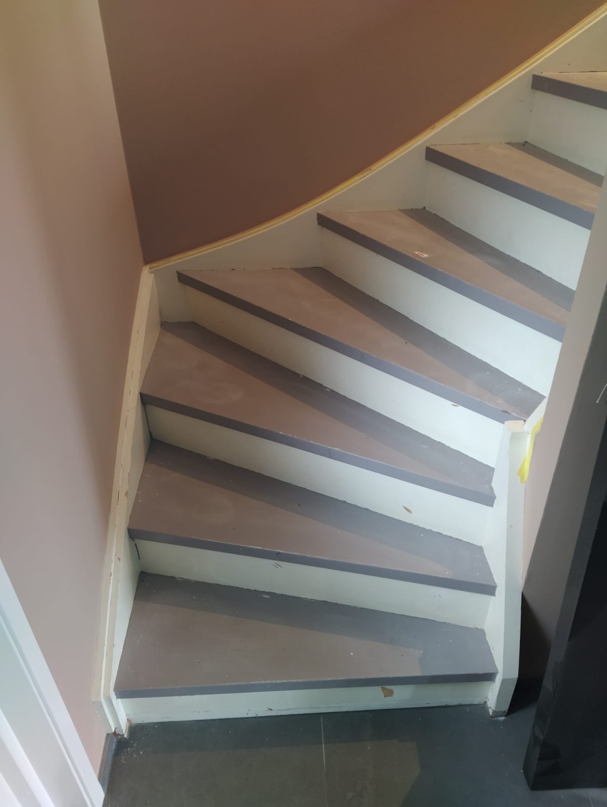 Drewniane schody wewnętrzne po malowaniu, z szarymi stopniami i białymi podstopnicami, widoczne ślady świeżej farby i taśma malarska zabezpieczająca.