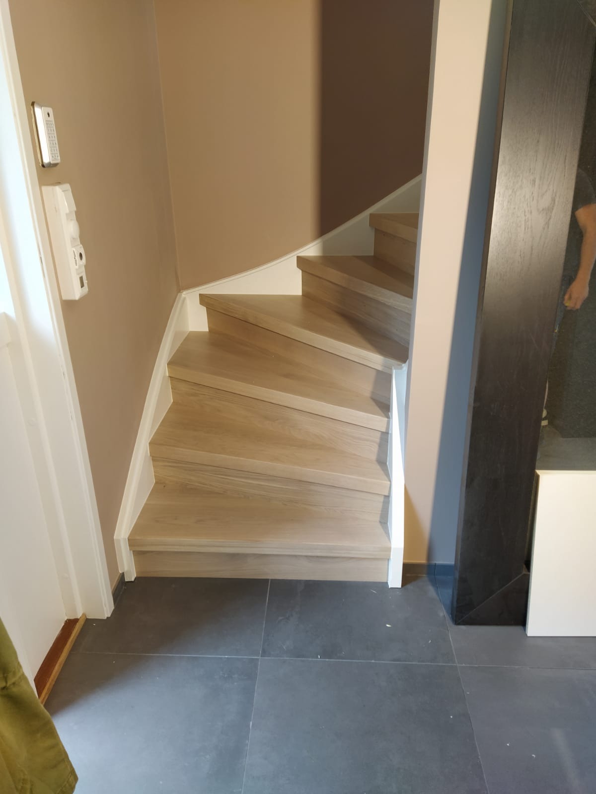 Jasne drewniane schody z białymi podstopnicami na ciemnej, kwadratowej posadzce, widok z dołu, obok ściana w odcieniach beżu i brązu.