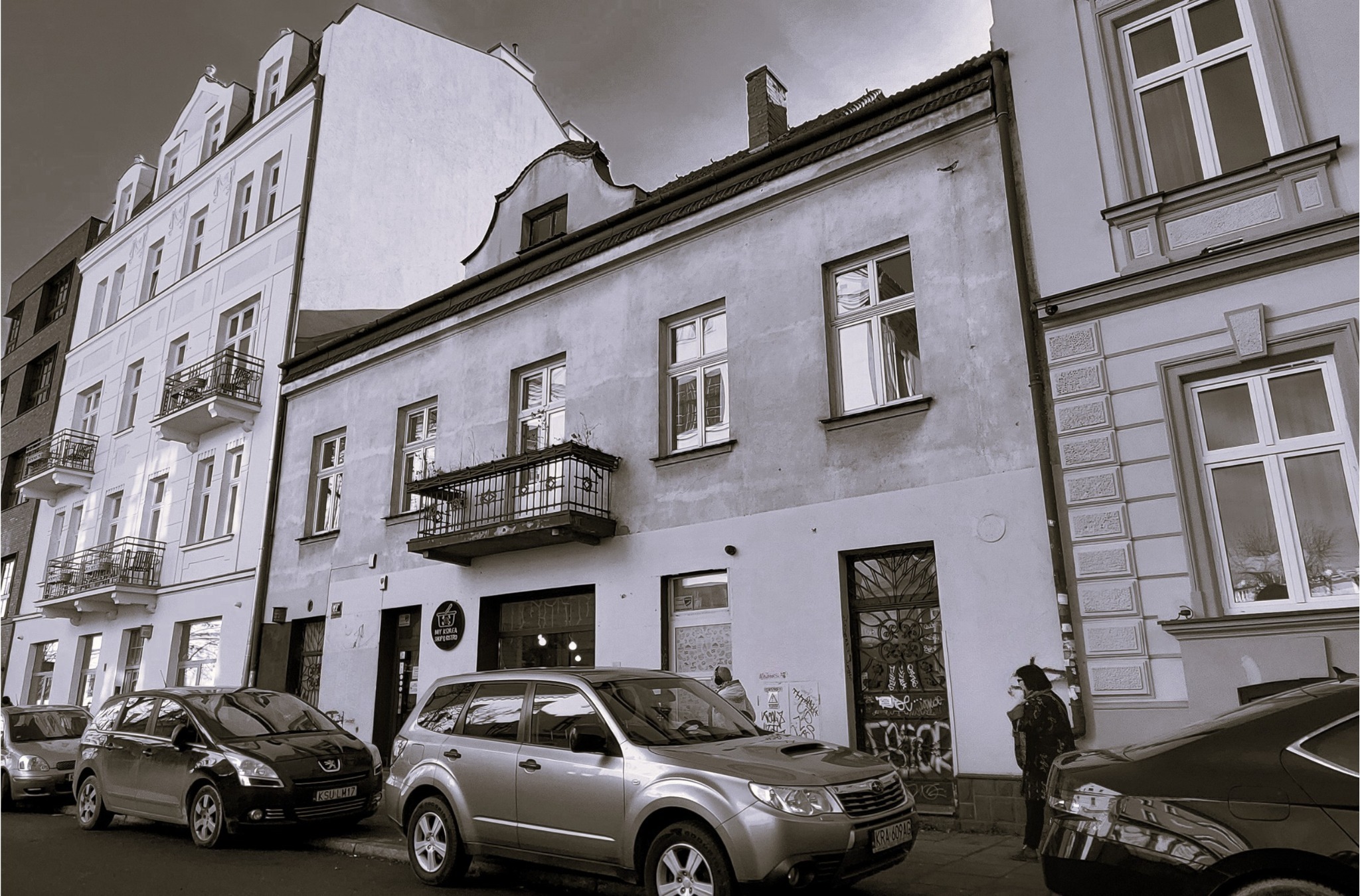 Kamienica w Krakowie z balkonami i ozdobnymi oknami, przed budynkiem zaparkowane samochody, widok z ulicy.