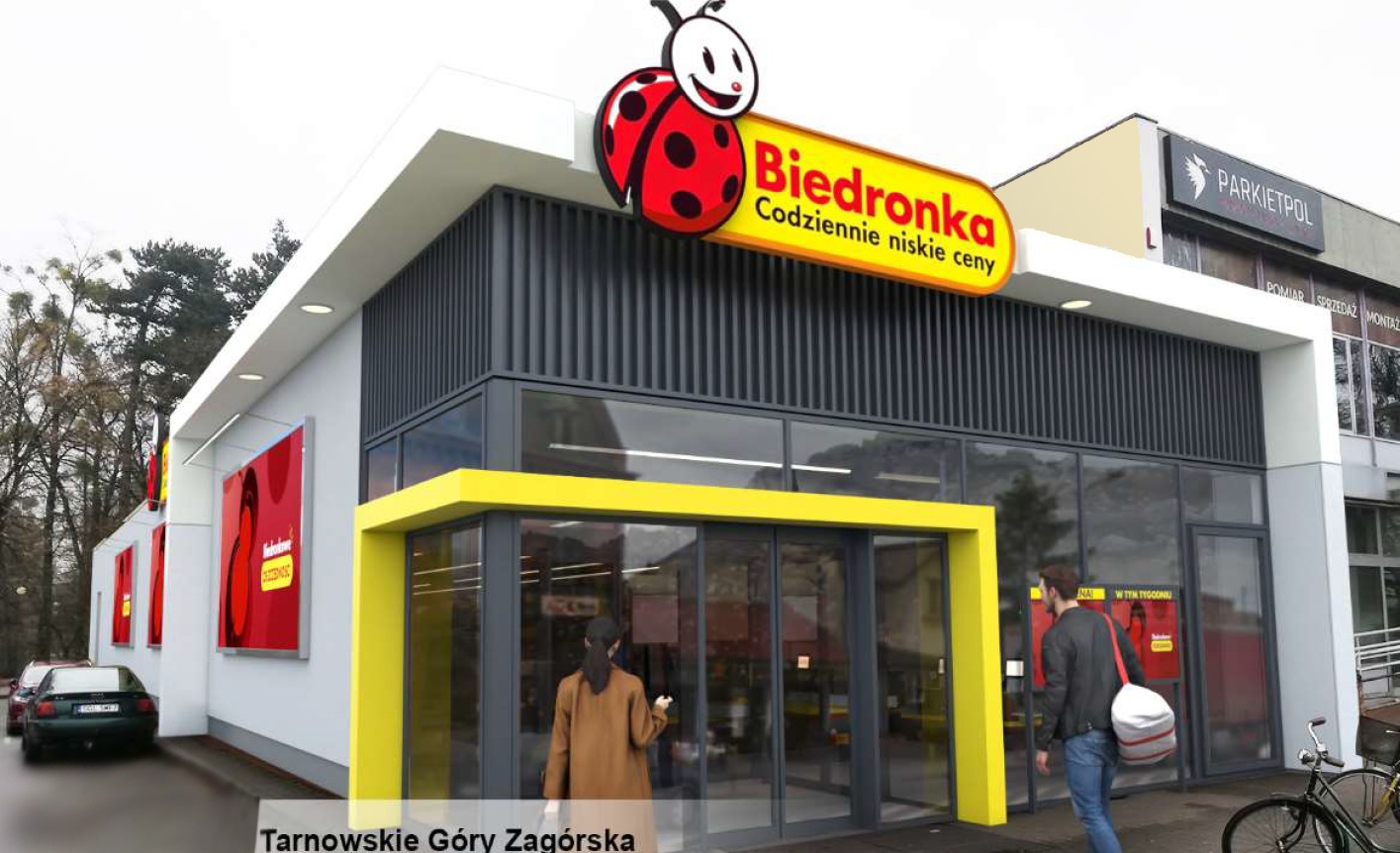 Fasada sklepu Biedronka z żółtym wejściem, widoczne osoby wchodzące i wychodzące, szyld z logo i hasłem 'Codziennie niskie ceny'.