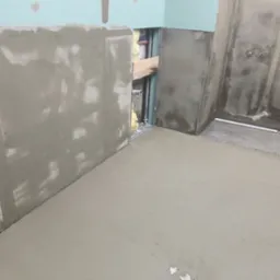 Wyrównana wylewka podłogowa w trakcie prac wykończeniowych w łazience, widoczne przygotowane ściany z instalacjami, surowy stan.