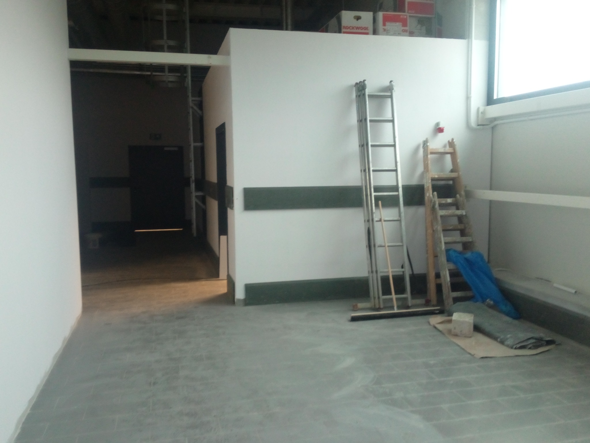 Wnętrze hali w trakcie prac wykończeniowych w Rudzie Śląskiej, widoczne dwie drabiny o różnej konstrukcji, zabezpieczone podłoże i ściany, surowe ściany i podłoga.