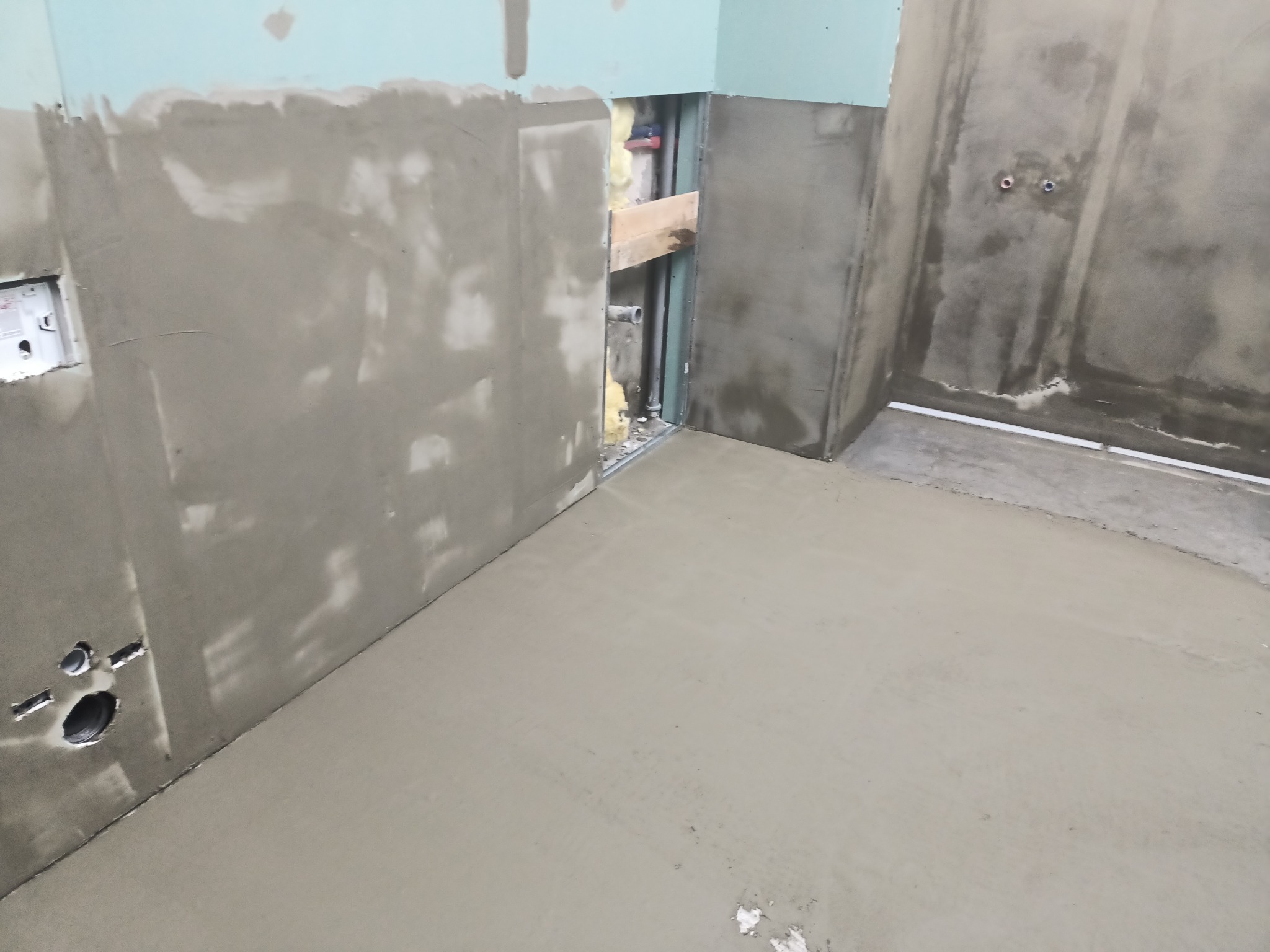 Wyrównana wylewka podłogowa w trakcie prac wykończeniowych w łazience, widoczne przygotowane ściany z instalacjami, surowy stan.