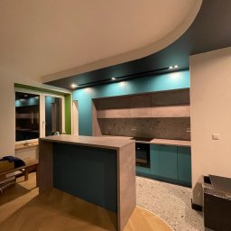 DTM - Nowoczesna kuchnia z wyspą, turkusowe szafki z szarym blatem i panelem, oświetlenie punktowe w podwieszanym suficie, parkiet w jodełkę i podłoga lastryko