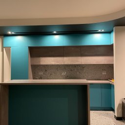 DTM - Nowoczesna kuchnia z wyspą, turkusowe i szare szafki, blat z szarego kamienia, parkiet w jodełkę.