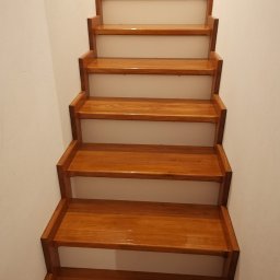 DTM - Polakierowane drewniane schody wewnątrz domu, widok od dołu, z materiałami budowlanymi na górnym podeście.