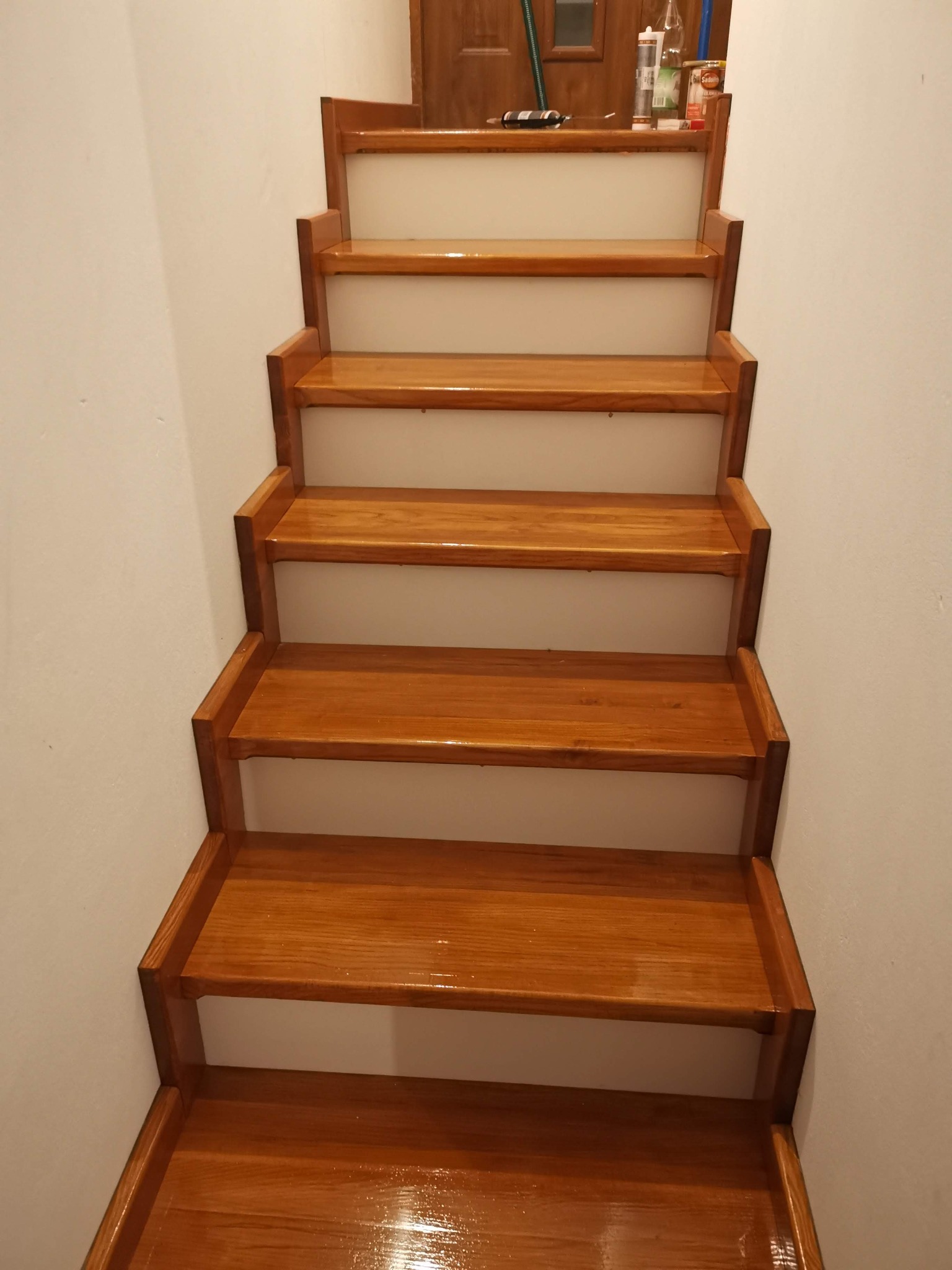 Polakierowane drewniane schody wewnątrz domu, widok od dołu, z materiałami budowlanymi na górnym podeście.