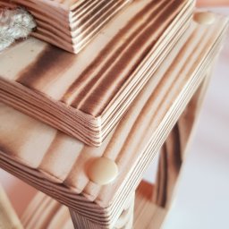 Adam Wasilewski - Drewniana konstrukcja z wypalanymi wzorami, połączona sznurkiem. Widoczne warstwy drewna i kremowe elementy mocujące. Ujęcie z góry, na jasnym tle.