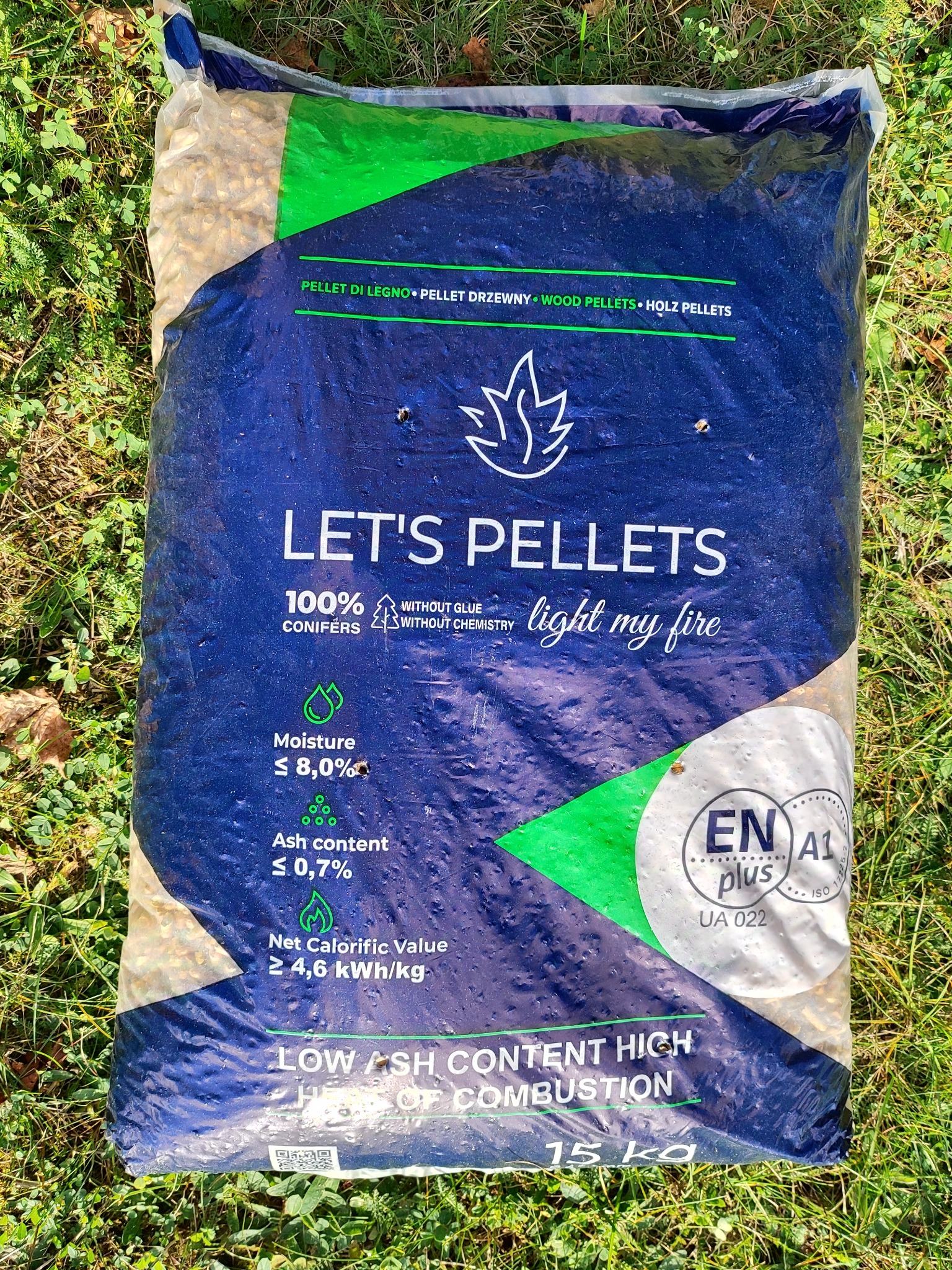Worek z pelletem drzewnym na trawie, widoczne informacje o produkcie: niska zawartość popiołu, wysoka wartość kaloryczna, certyfikat EN A1 plus.